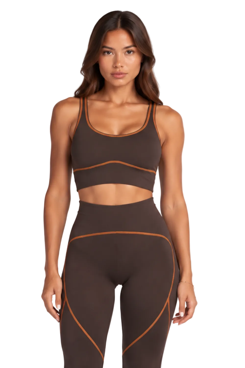 A woman modeling a matching dark brown activewear set consisting of a sports bra and high-waisted leggings with contrasting orange-brown piping details, paired with white sneakers against a plain white studio background.