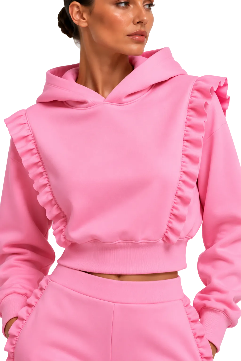 A woman wearing a bright pink cropped hoodie with dramatic ruffle details on the shoulders and front, paired with matching pink ruffle-trimmed pants, against a clean white studio background.