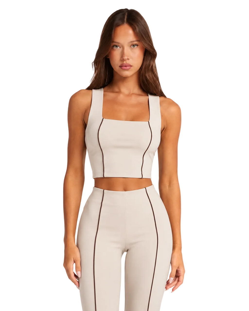 A woman modeling a matching beige two-piece activewear set with dark contrast stitching, featuring a cropped tank top and high-waisted leggings, against a plain white background.