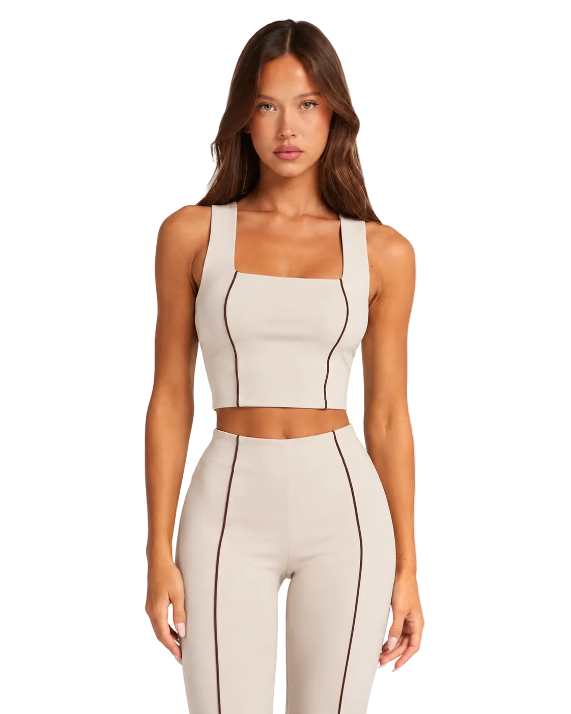 A woman modeling a matching beige two-piece activewear set with dark contrast stitching, featuring a cropped tank top and high-waisted leggings, against a plain white background.