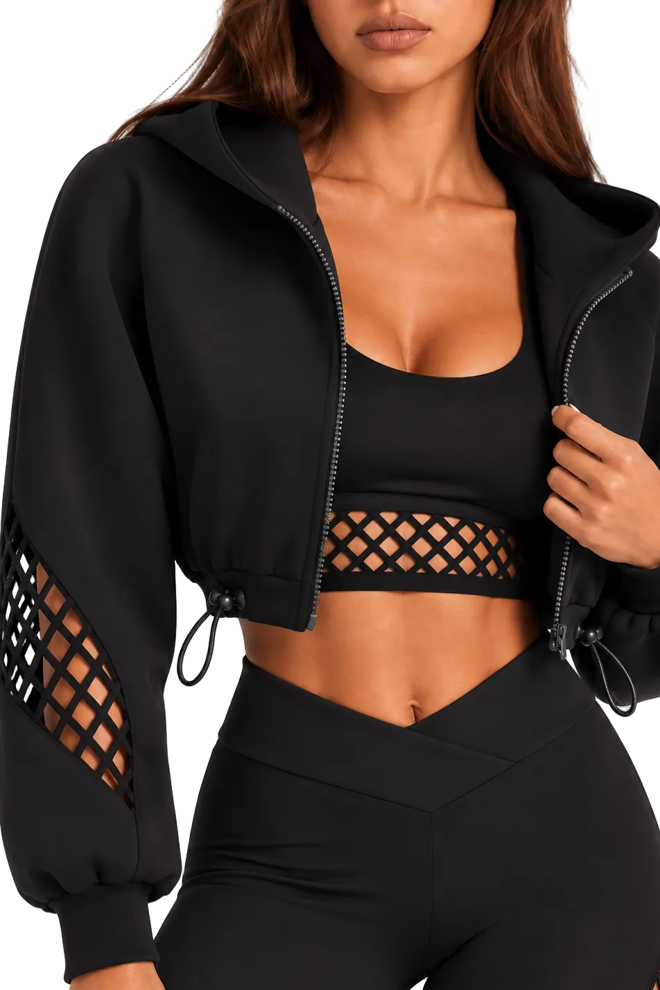 A woman wearing a black cropped zip-up hoodie with long sleeves, drawstring hem, and lattice cutout details on the sleeves, paired with matching black activewear.