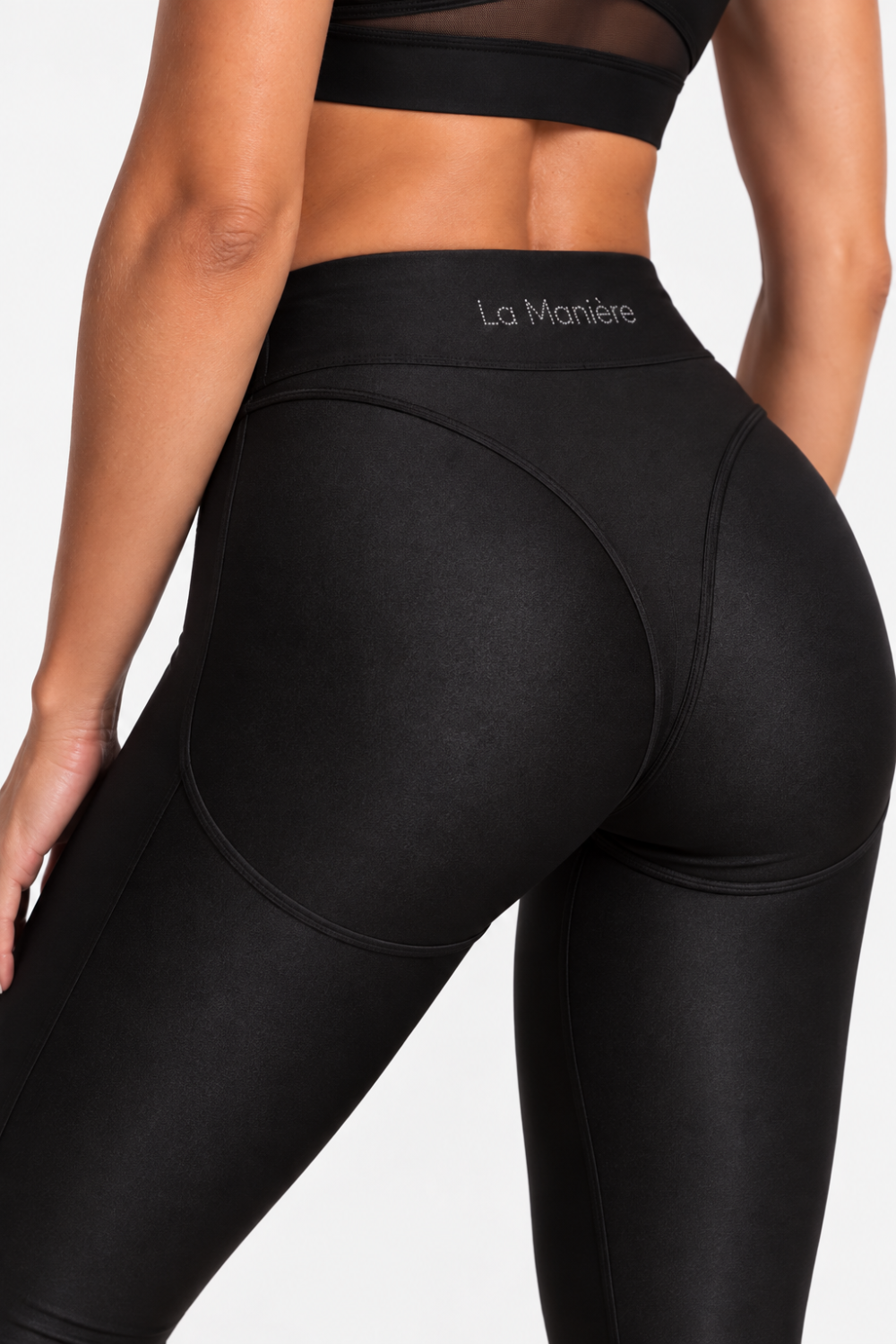 Close-up back view of a model wearing black high-waisted leggings with a visible La Marchée waistband logo, against a plain light background.